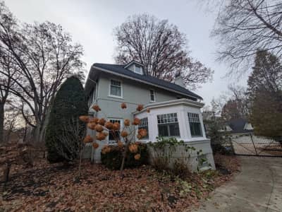 White house exterior with dormer window and autumn foliage in the landscape.