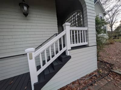 White house exterior with entry door, white railing, and dark stairs.