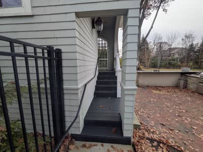 House exterior with wooden deck railing and black stairs leading down.