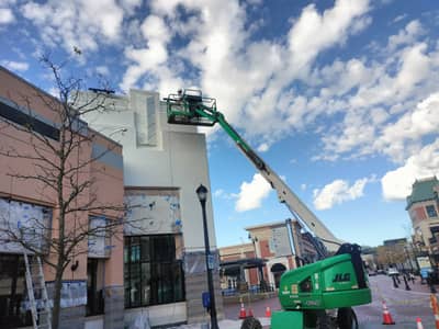 Commercial building with green aerial lift positioned against the white facade.