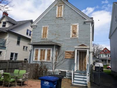 House exterior with white siding and boarded-up window openings.