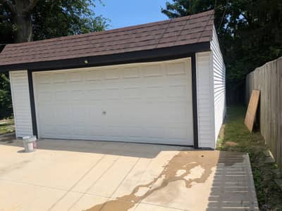 Detached garage with gray overhead door and brown roof.