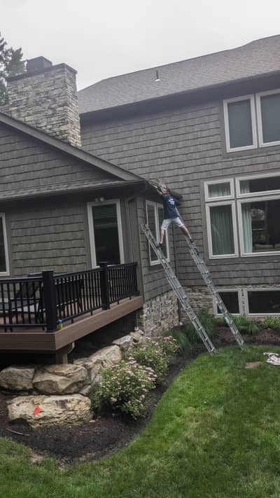 House exterior with gray shingle siding, ladder in position, and stone chimney.