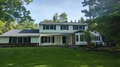 Large two-story colonial house with light green-tinted exterior and centered entry.