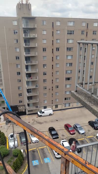 Tall concrete apartment building with balconies overlooking a parking area.