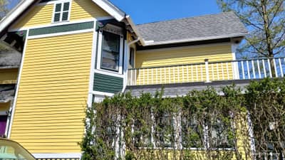 Yellow house with dark roof and white porch railings.