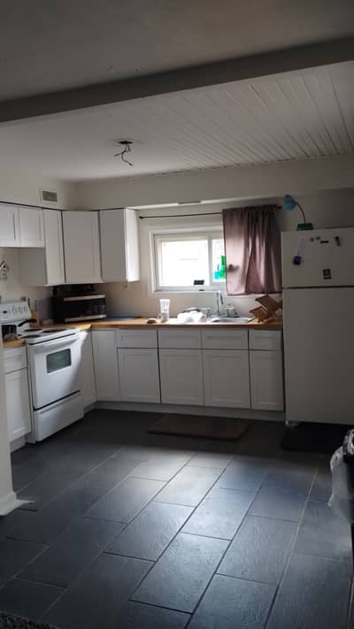 Kitchen with white cabinets, dark tile floor, and dark ceiling beam.