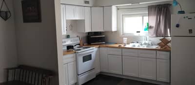 Kitchen with white cabinets, stove, refrigerator, and window view.