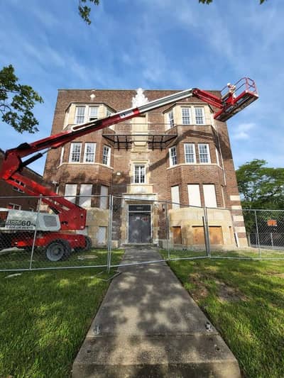 Large brick building with red scissor lift for painting or maintenance.