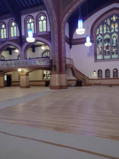 Interior of a religious building with ornate arched stained glass windows and wooden flooring.