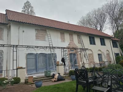 Exterior of a Mediterranean-style white house with ladders and construction materials present.