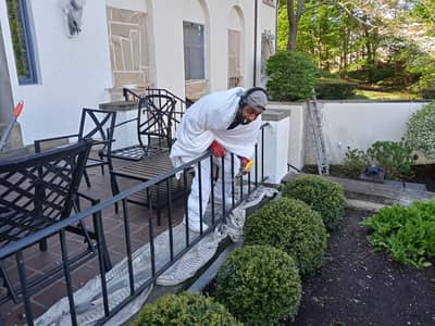 Exterior of a white residential building with a worker painting deck railings.