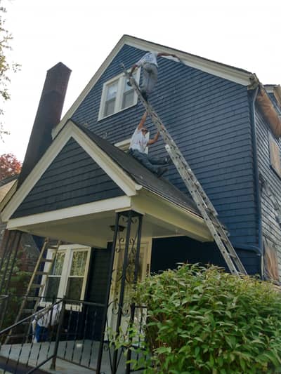 Exterior of residential house with blue siding and roof with person on ladder.