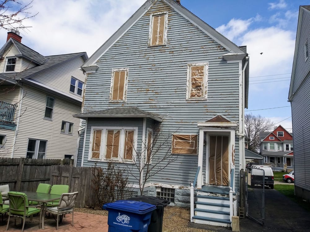 Light blue painted house with boarded windows and visible work in progress.