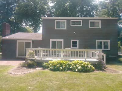 Olive green painted house with white covered porch and foundation plantings.
