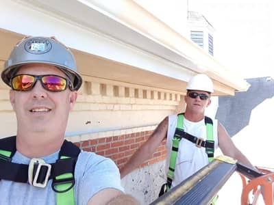 Two construction workers in safety equipment working on exterior trim and siding.