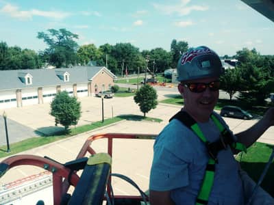 Worker on aerial lift with residential structures and landscaping visible below.