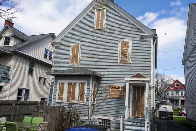 A clapboard house mid-preparation, with bare wood patches and windows masked off.