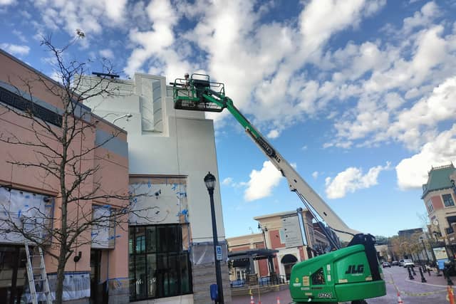 A boom lift raised against a commercial building being repainted, with sections masked off.