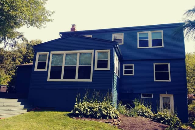 A deep blue house with a white-trimmed sunroom of tall windows.