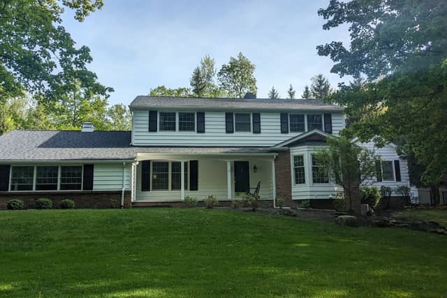 A pale green colonial house with white trim and dark shutters.