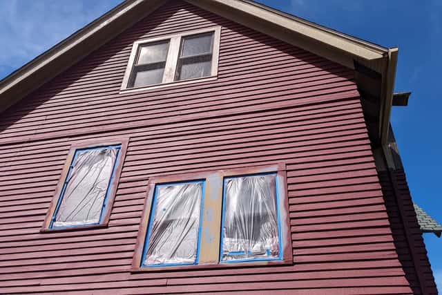 A red clapboard gable with windows sealed under plastic and blue tape.