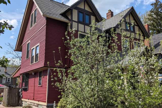 A deep red clapboard house beside a Tudor gable, with a flowering tree in front.
