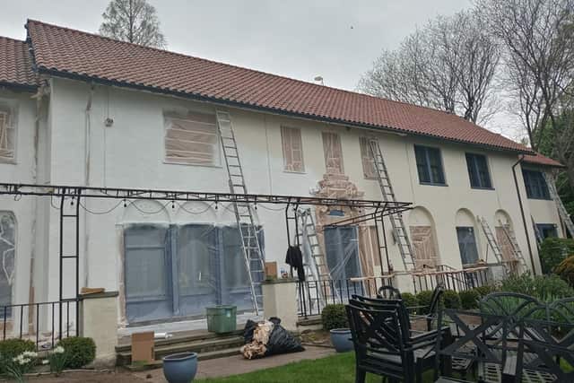 A stucco house under preparation, with ladders up and windows covered in masking paper.