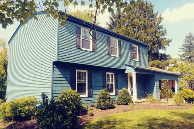 A teal-blue colonial house with white window trim and dark shutters.