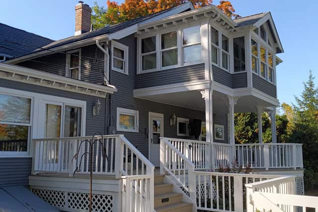 A grey Victorian porch with white spindle railings, brackets and a bay window above.