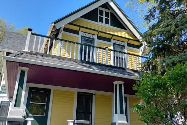 The upper balcony of a yellow house with green trim and white spindle railings.