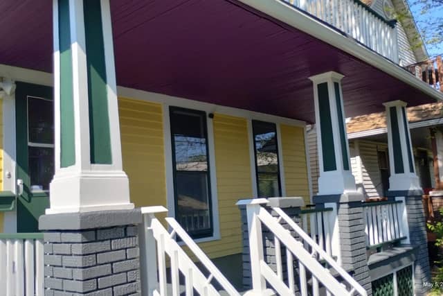 A porch with a deep purple ceiling, green and white columns and yellow siding.