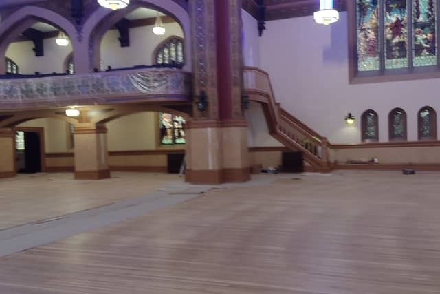 A historic hall with a painted staircase, arched balcony and stained glass windows.