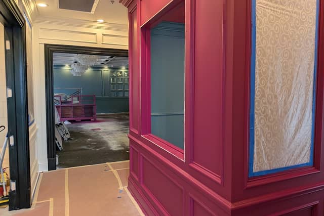 Raspberry-painted panelling beside a teal room, with the floor papered and edges masked.